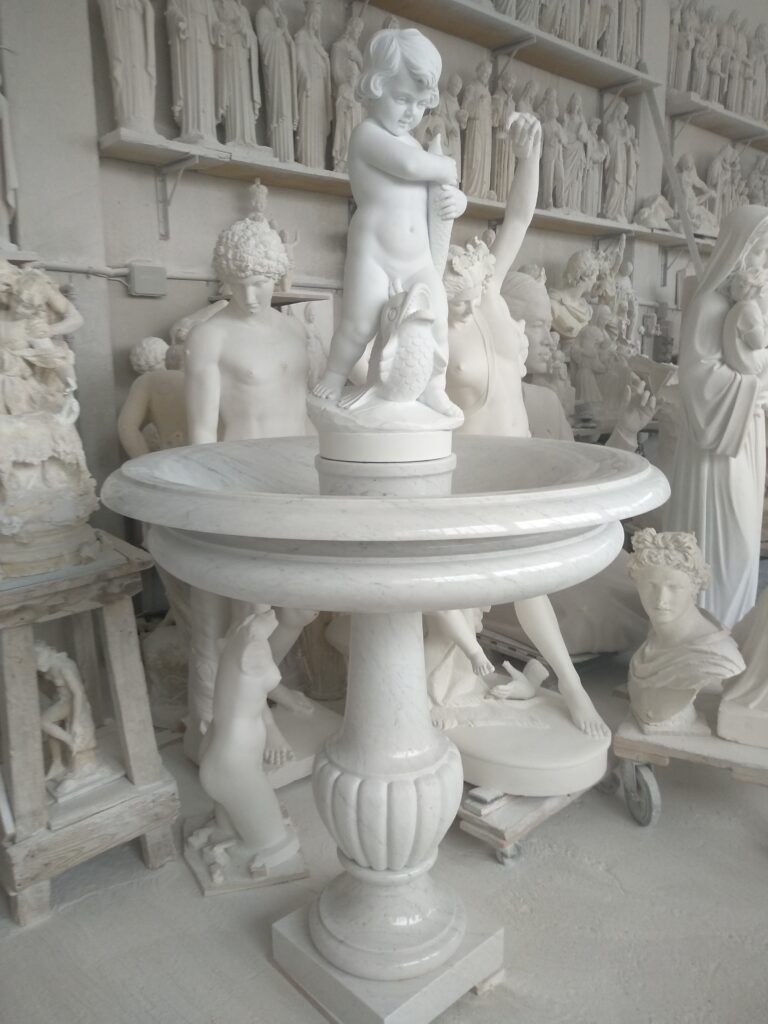 Hand-carved marble fountain with a cherub and fish sculpture inside Studio Giannoni atelier